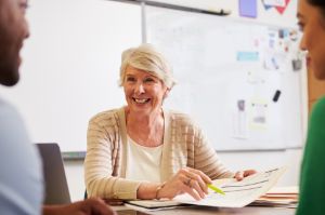 Ältere Lehrerin spricht mit Studenten am Schreibtisch über Erwachsenenbildung 