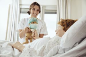 Ein Junge liegt im Krankenhausbett und die Ärztin gibt ihm einen Teddy.