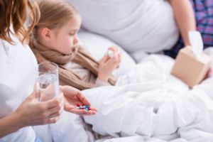 Ein Kind liegt im Bett und bekommt Tabletten und ein Glas Wasser von seiner Mutter gereicht.