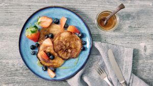 Pancakes und Obst auf einem Teller mit Besteck daneben und einem Glas Honig.