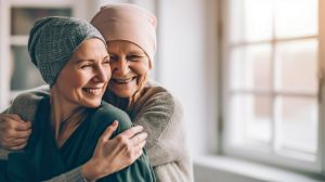 Eine junge und eine ältere Krebspatientin umarmen sich herzlichen und lächeln dabei.