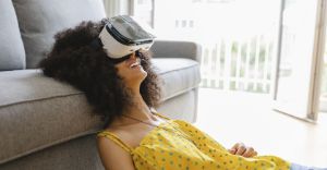 Frau mit Virtual Reality Brille liegt auf dem Boden mit dem Kopf auf der Couch.
