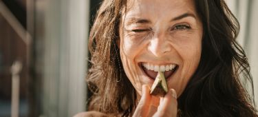 Frau beißt lachend und zwinkernd in eine Avocado.