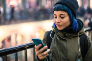 Mädchen mit blauen Haare schaut auf ein Handy.