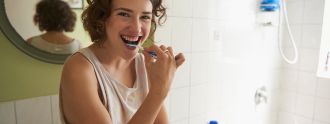 Eine junge Frau mit Locken steht im Bad und putzt sich fröhlich die Zähne. 
