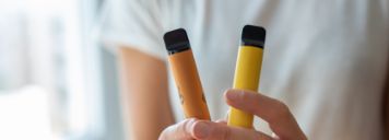 Eine Person hält zwei gelbe E-Zigaretten in den Händen.