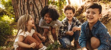 Vier Kinder sitzen zusammen vor einem Baum.